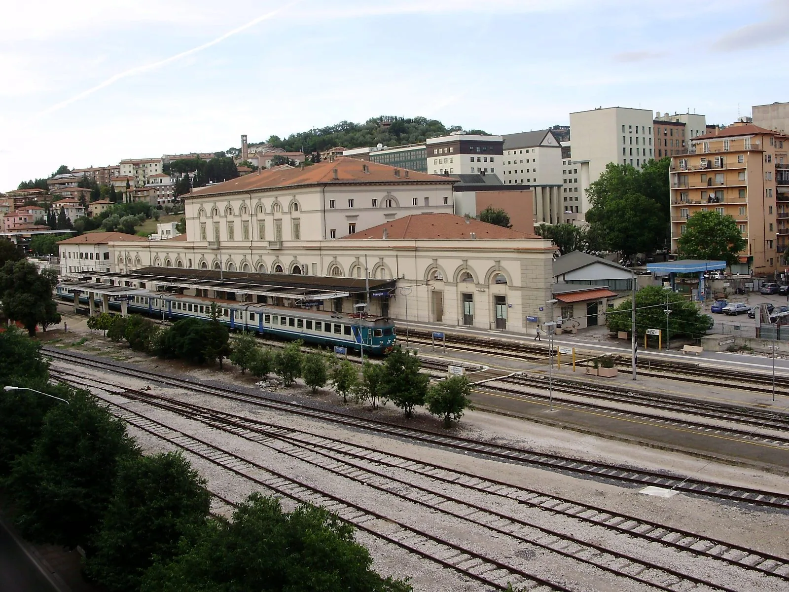 La stazione ferroviaria di Perugia Fontivegge vista dall'alto, con un treno regionale fermo al binario e la città sulla collina alle spalle