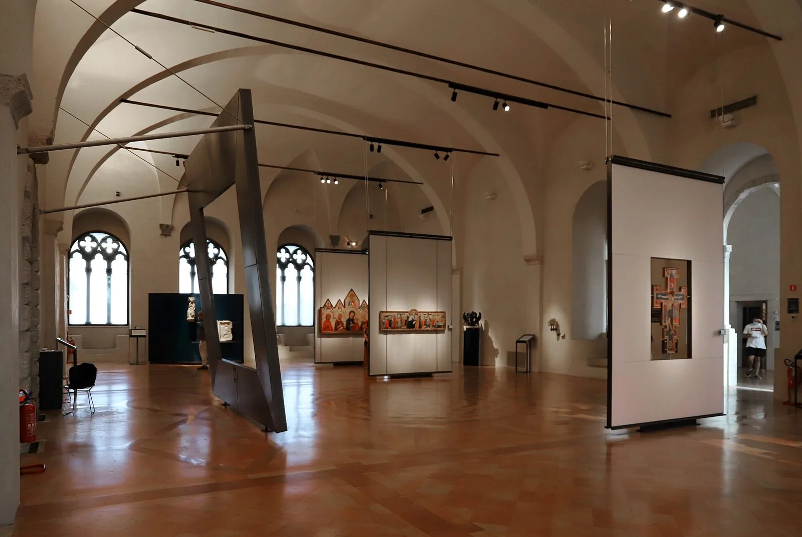 Una sala della Galleria Nazionale dell'Umbria a Perugia con volte a crociera, finestre gotiche, pannelli espositivi sospesi e dipinti su tavola medievali