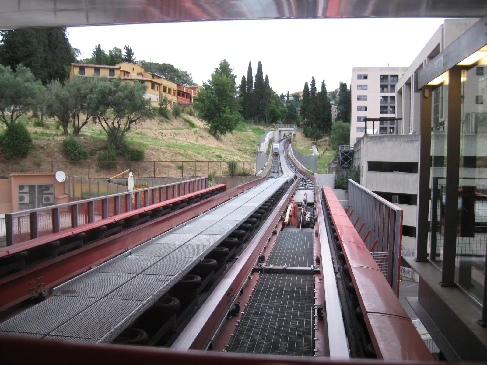 Il binario rosso del Minimetrò di Perugia che sale verso la collina, con una vettura in arrivo tra ulivi e cipressi